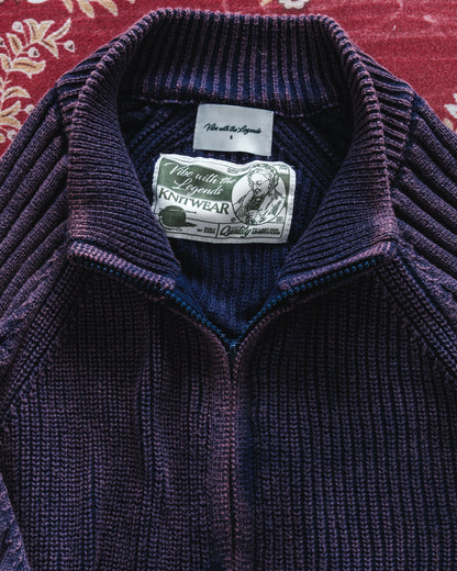 Close-up of a purple knit sweater with a brand label on a red patterned background