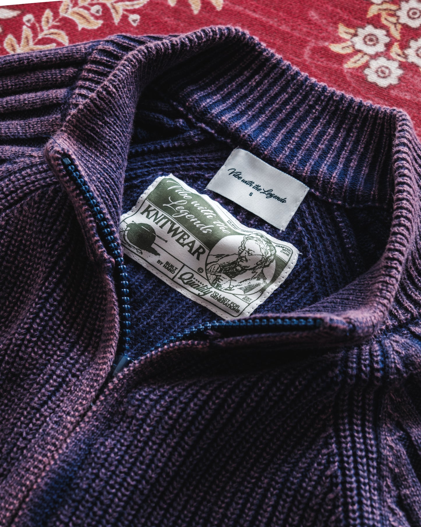 Close-up of a purple knit sweater with a brand label on a red floral background