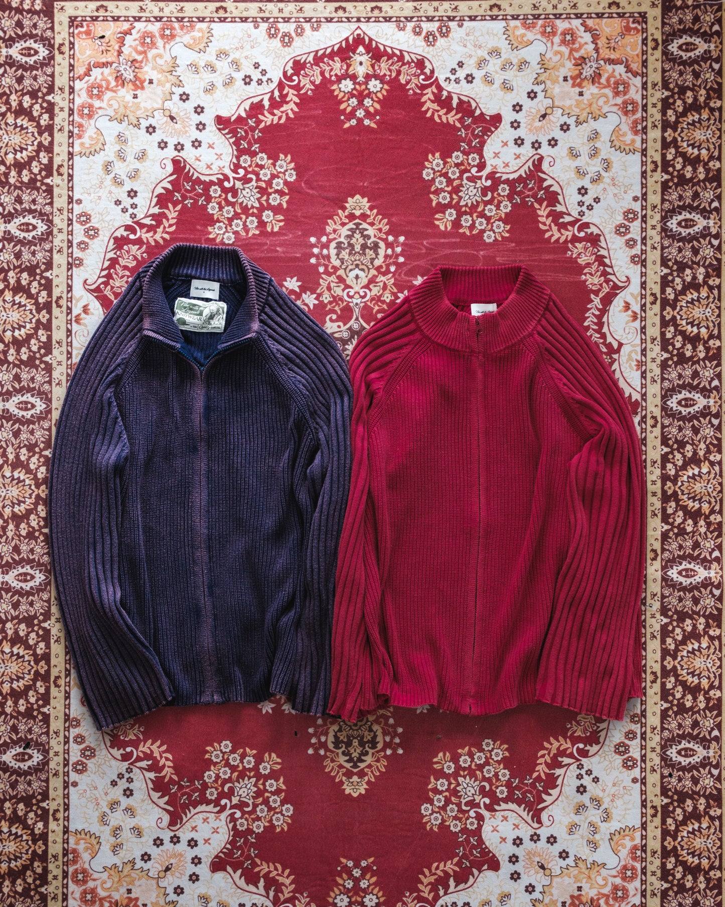 Two sweaters, one purple and one red, on a patterned rug.